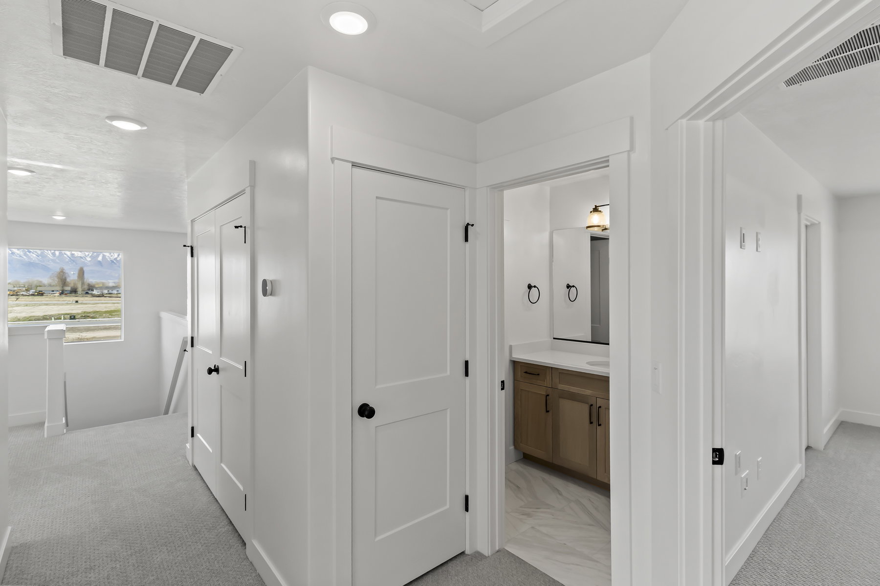 Hallway featuring light gray carpeting, white walls, recessed lighting, and a window with mountain scenery