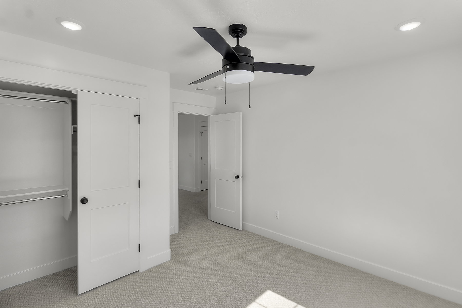 Neutral tone bedroom featuring a black ceiling fan with integrated lighting, recessed ceiling lights, a double-door closet with shelving and hanging rods, and light-colored carpeting