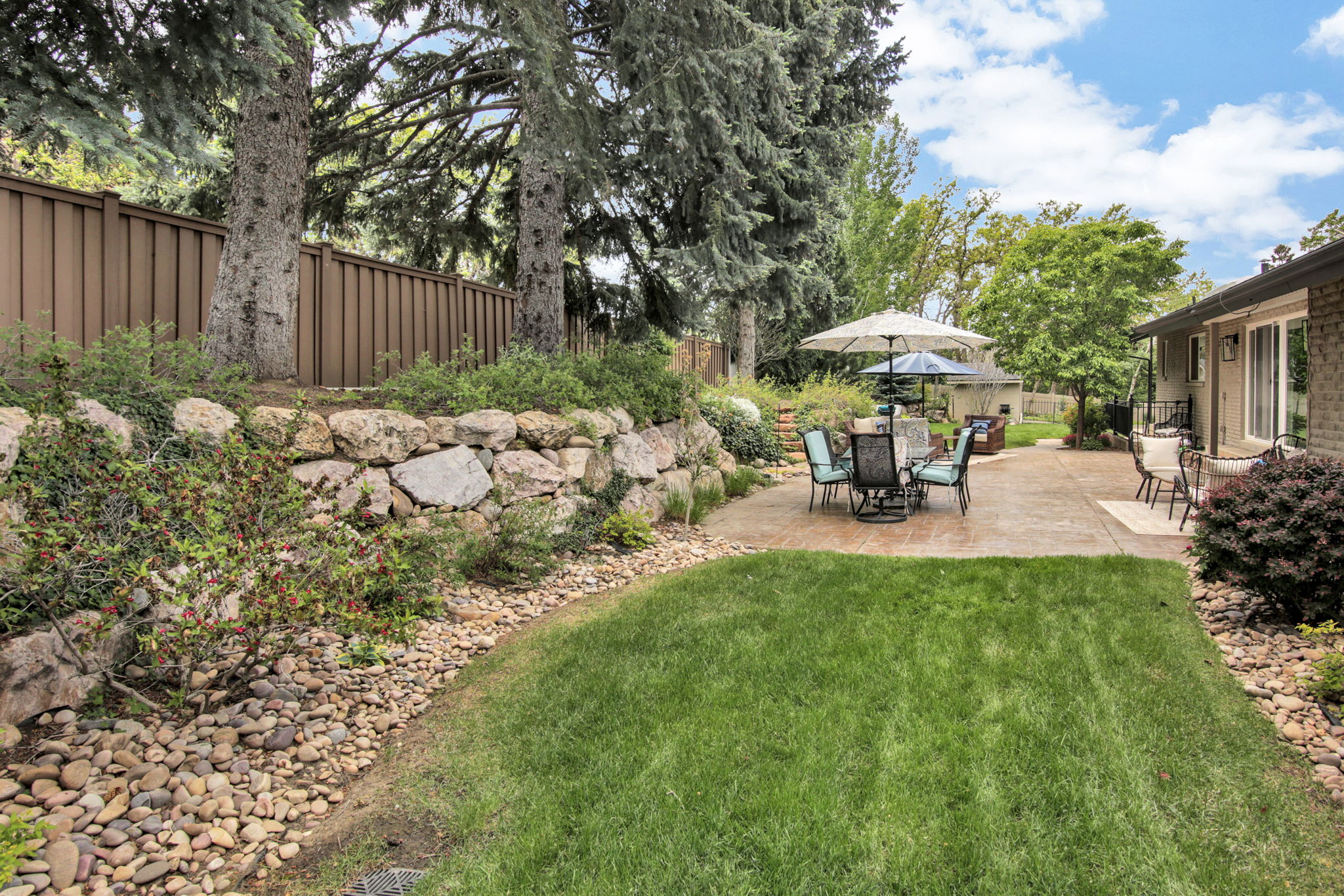 Expansive backyard featuring a manicured lawn, a large stamped concrete patio, and a stone retaining wall