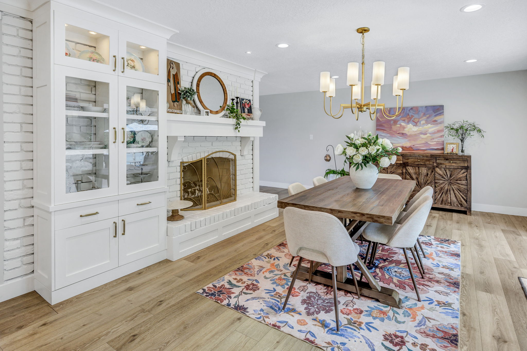 Dining area featuring wood-finish flooring, a white brick fireplace with a mantel, and built-in white cabinetry with glass display doors