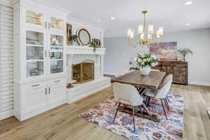 Dining area featuring wood-finish flooring, a white brick fireplace with a mantel, and built-in white cabinetry with glass display doors