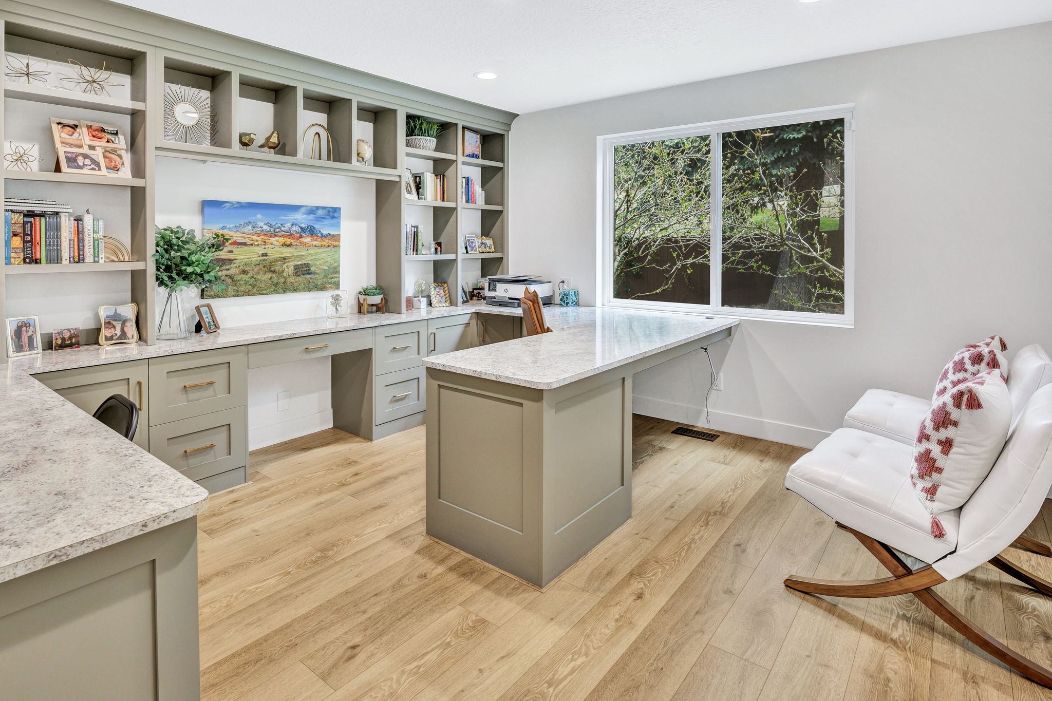 Dedicated workspace featuring extensive built-in cabinetry, substantial counter surfaces, wood-finish flooring, a generous window, and recessed lighting