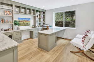 Dedicated workspace featuring extensive built-in cabinetry, substantial counter surfaces, wood-finish flooring, a generous window, and recessed lighting