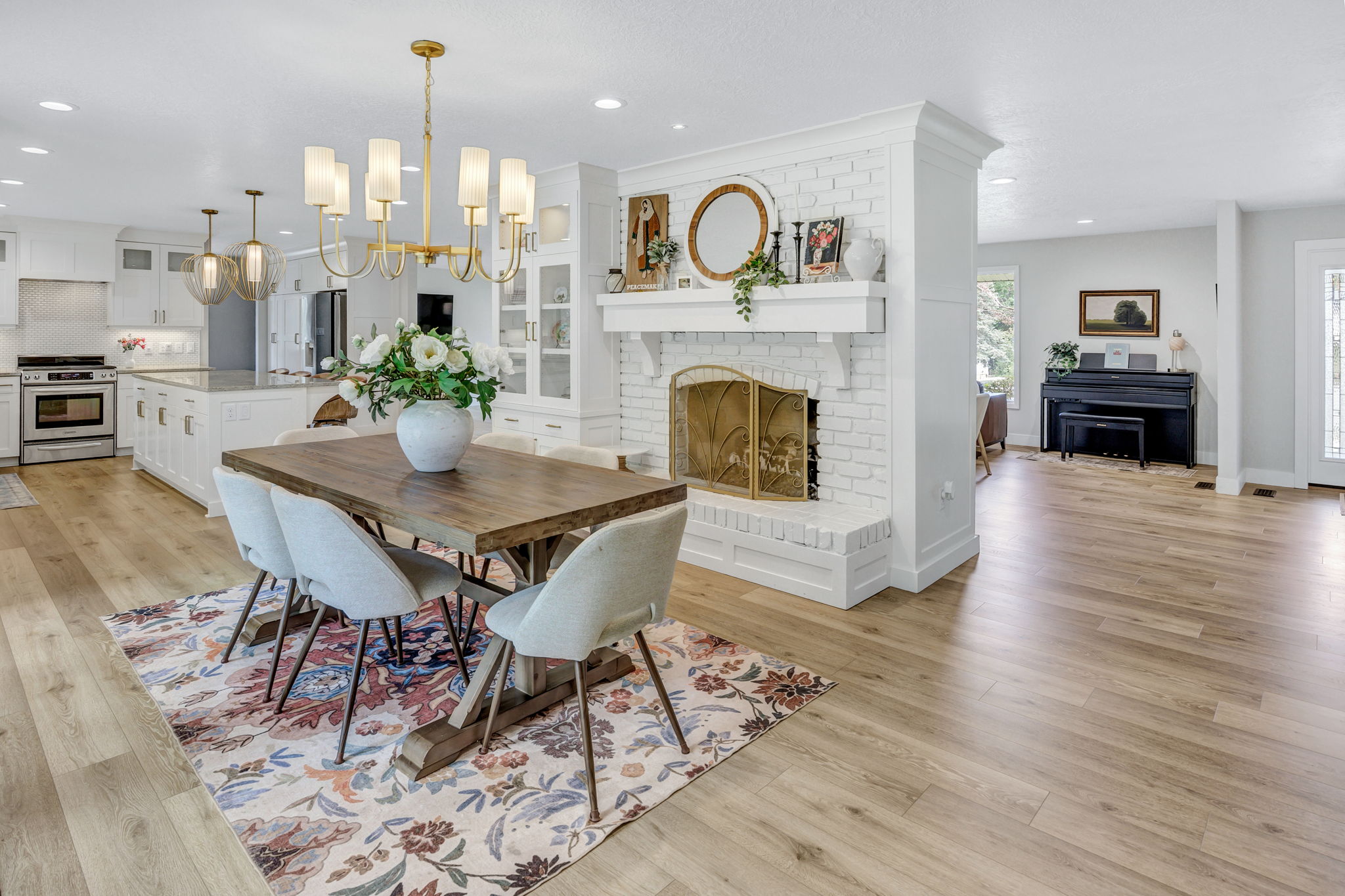 Open-concept living area featuring wood-finish flooring throughout, a white brick fireplace with a substantial mantel, and a formal dining space