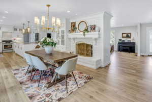 Open-concept living area featuring wood-finish flooring throughout, a white brick fireplace with a substantial mantel, and a formal dining space