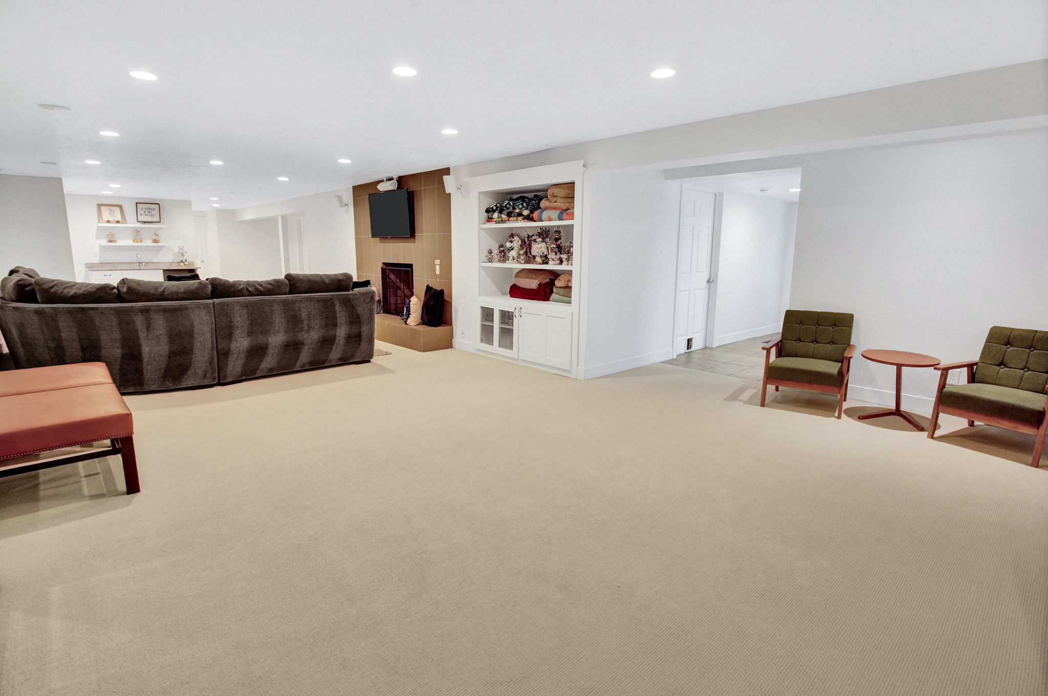Spacious recreation room featuring recessed lighting, a built-in entertainment center with a wood-finish accent wall, and a dedicated wet bar area with open shelving