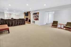 Spacious recreation room featuring recessed lighting, a built-in entertainment center with a wood-finish accent wall, and a dedicated wet bar area with open shelving