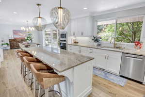 Open-concept kitchen featuring a large island with seating, pendant lighting, white cabinetry, a tiled backsplash, and stainless steel appliances
