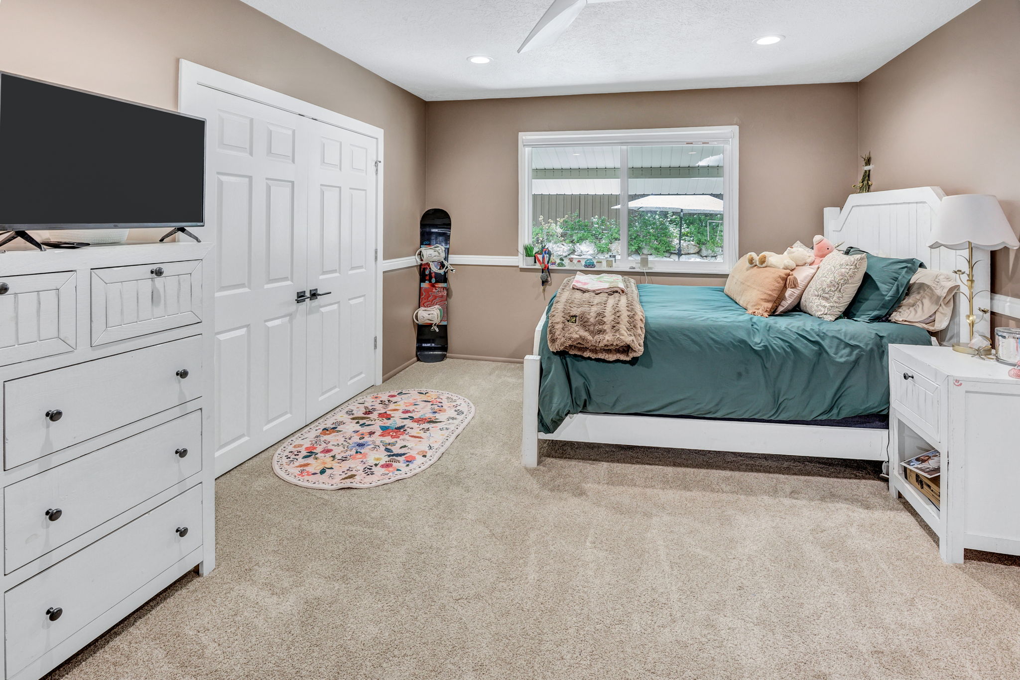 Carpeted room with neutral-toned walls, featuring a window with exterior views, white paneled double doors, recessed lighting, and a ceiling fan