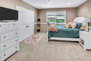 Carpeted room with neutral-toned walls, featuring a window with exterior views, white paneled double doors, recessed lighting, and a ceiling fan