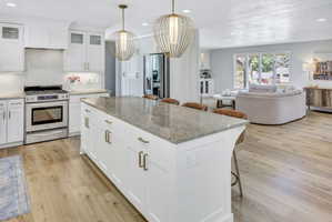 Kitchen featuring a large center island with a stone countertop, white shaker cabinetry with brass hardware, and wood-finish flooring