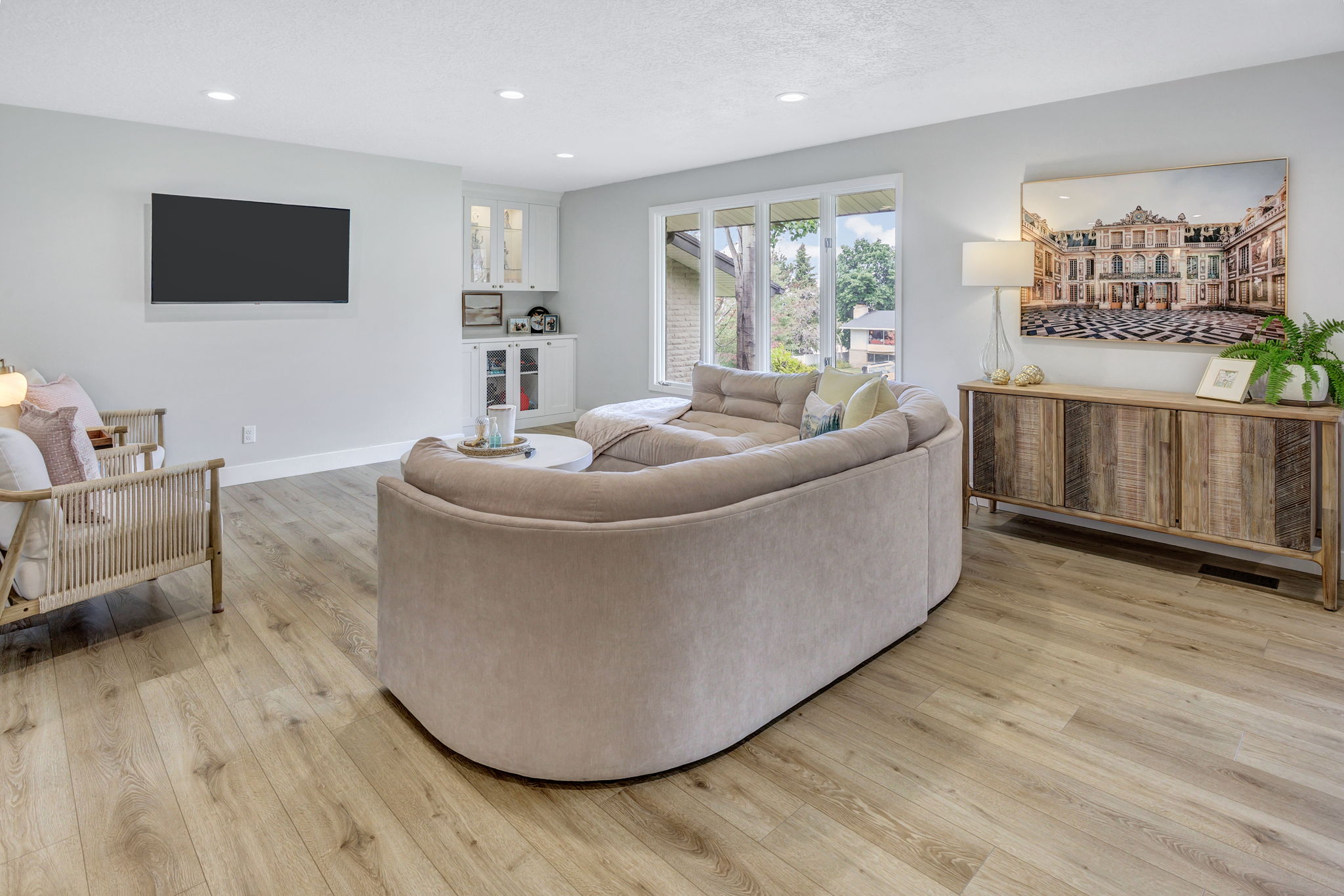 Open-concept living area featuring wood-finish flooring, a built-in beverage bar with glass-front cabinetry, recessed lighting, and expansive windows