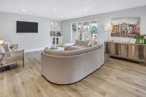 Open-concept living area featuring wood-finish flooring, a built-in beverage bar with glass-front cabinetry, recessed lighting, and expansive windows