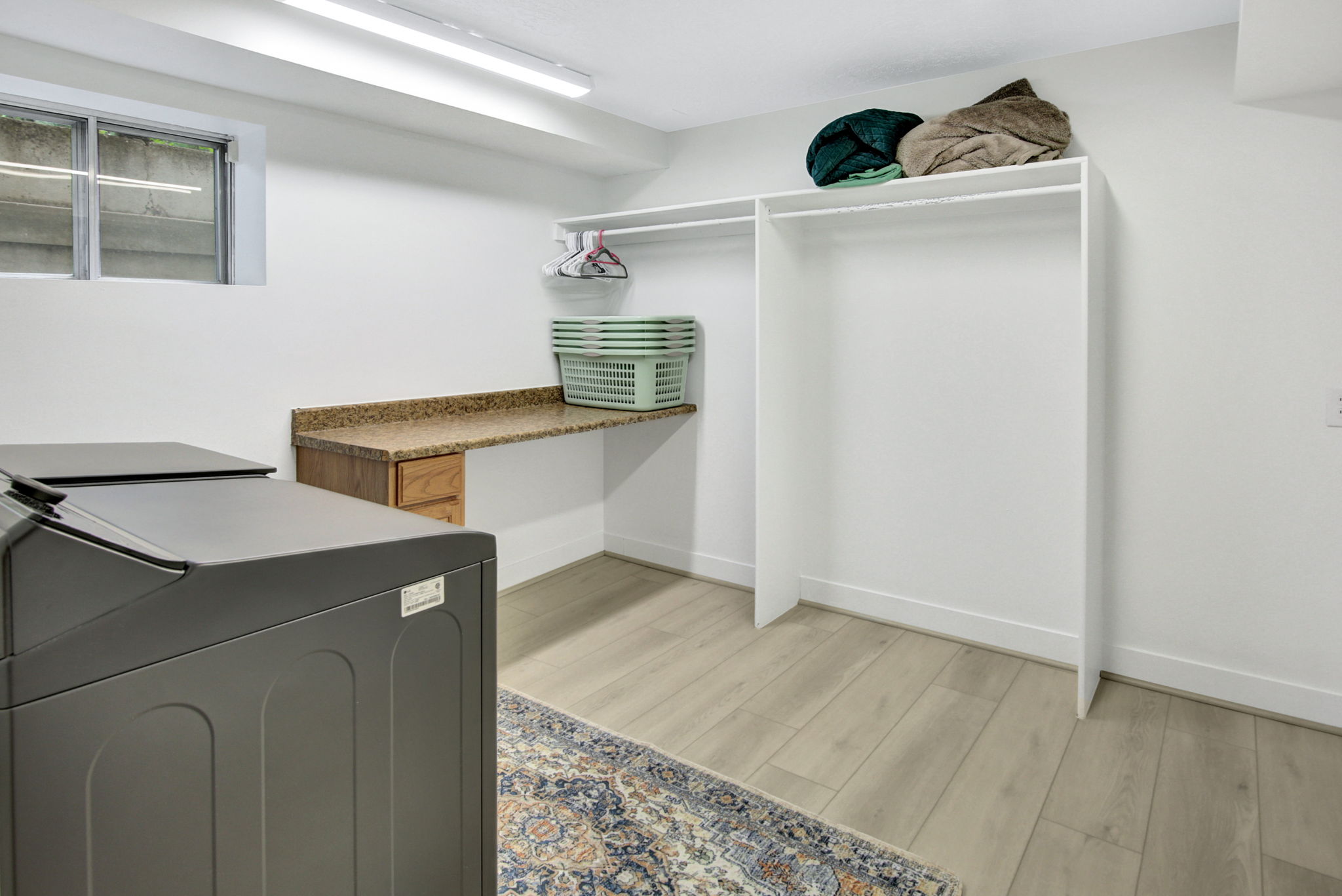 Laundry area featuring wood-finish flooring, a built-in counter with a stone-finish surface, integrated wood-finish cabinetry, and overhead fluorescent lighting