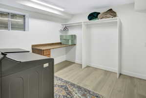Laundry area featuring wood-finish flooring, a built-in counter with a stone-finish surface, integrated wood-finish cabinetry, and overhead fluorescent lighting