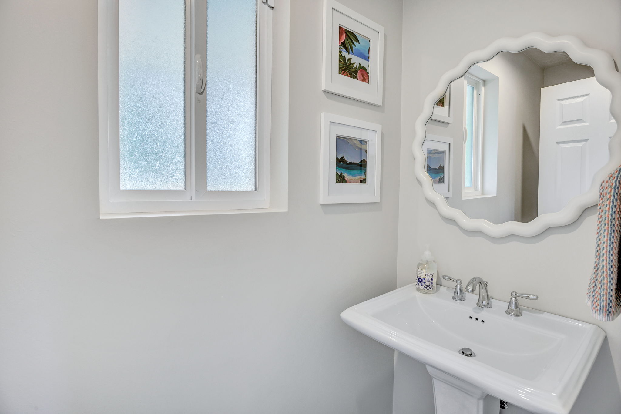 Pedestal sink with chrome-finish faucet and white scalloped mirror