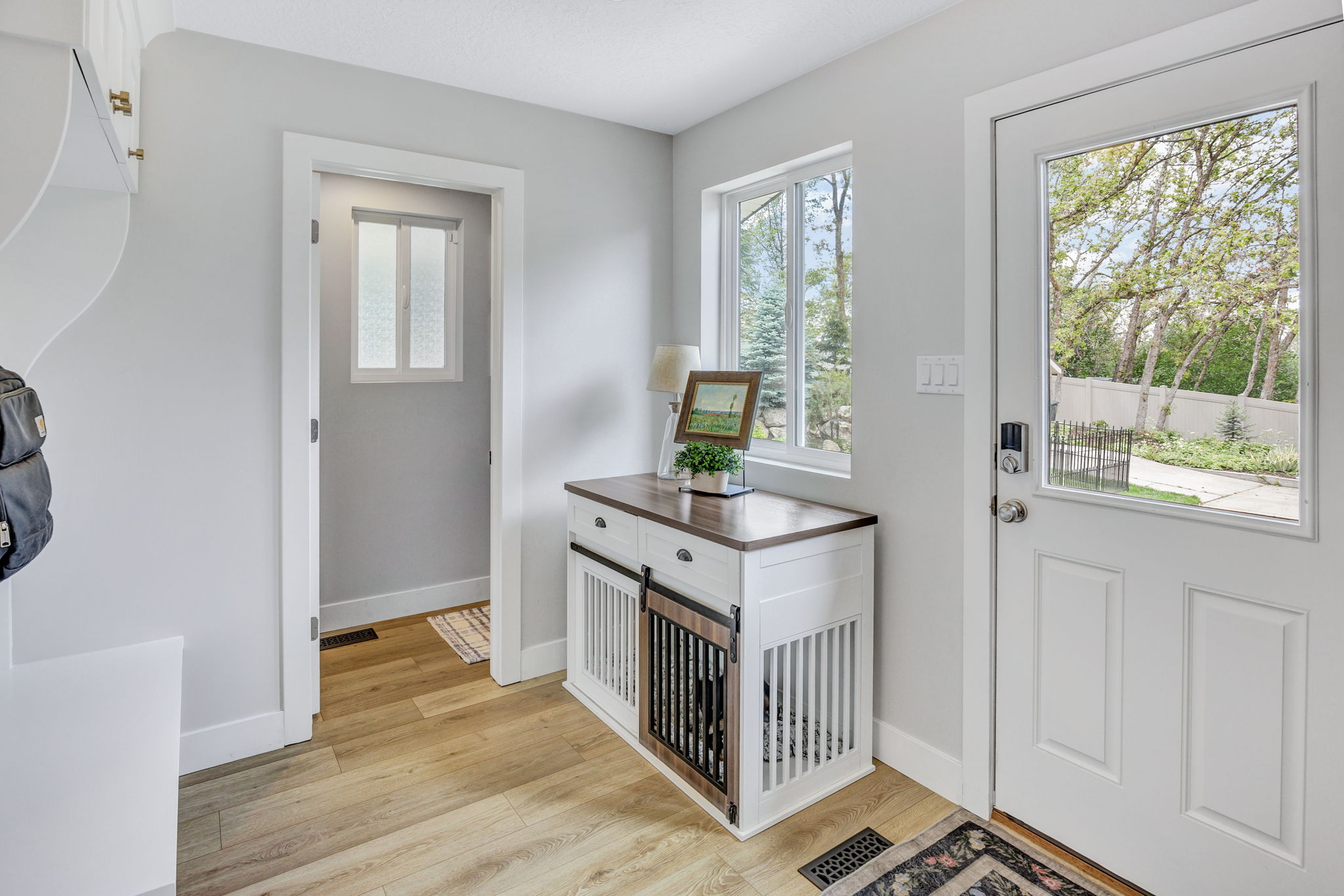 Entryway featuring a white paneled door with a glass insert, wood-finish flooring, light grey walls, and a built-in white storage bench with brass hardware