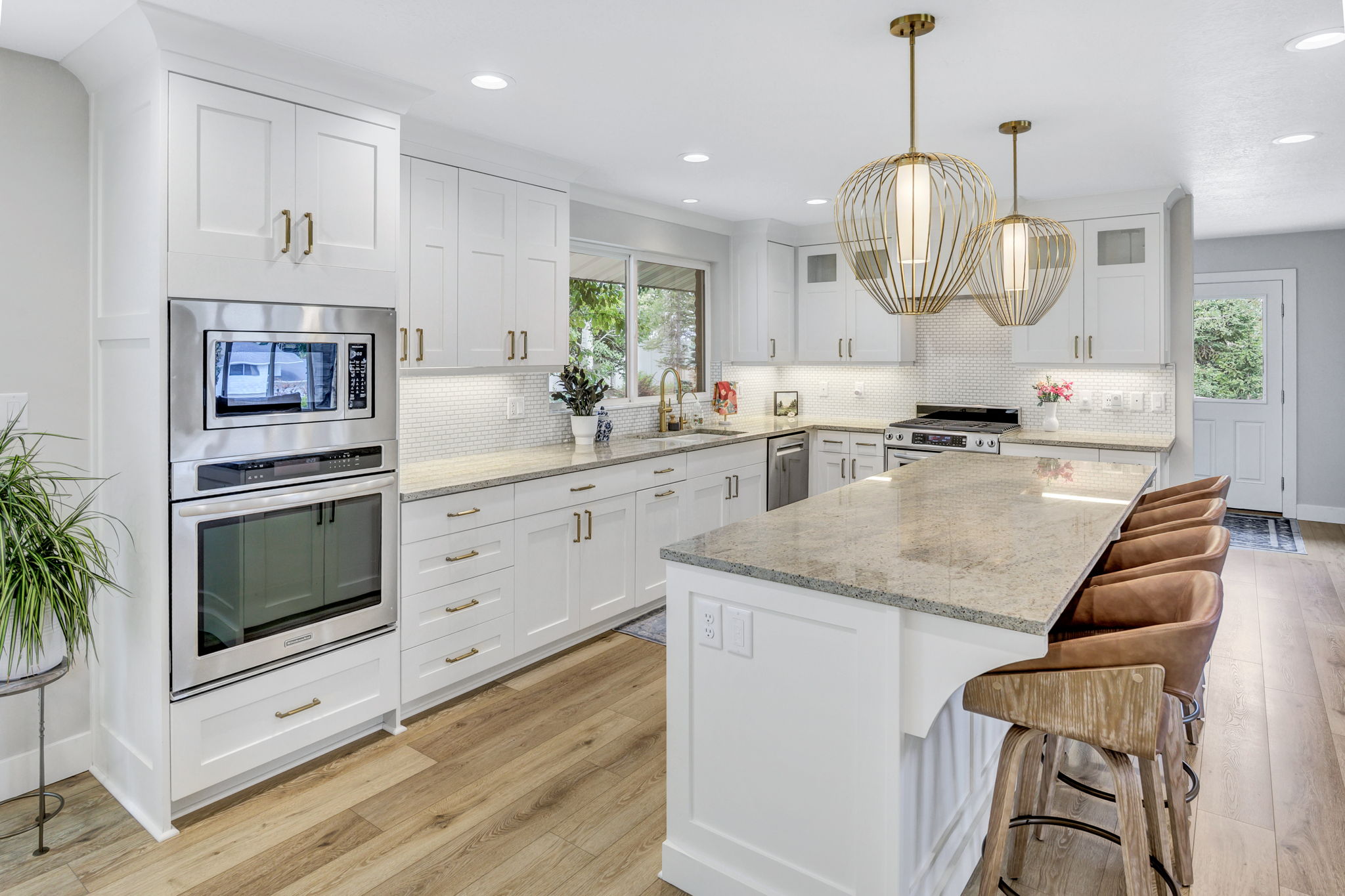 Kitchen featuring a large island with stone countertop, white shaker cabinetry, stainless steel built-in appliances, decorative pendant lighting, and wood-finish flooring