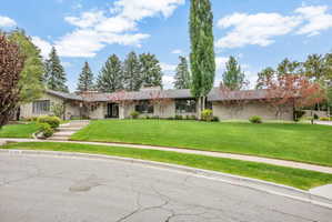 Contemporary ranch-style residence featuring a stone and stucco facade, a dark shingle roof, and an expansive front lawn