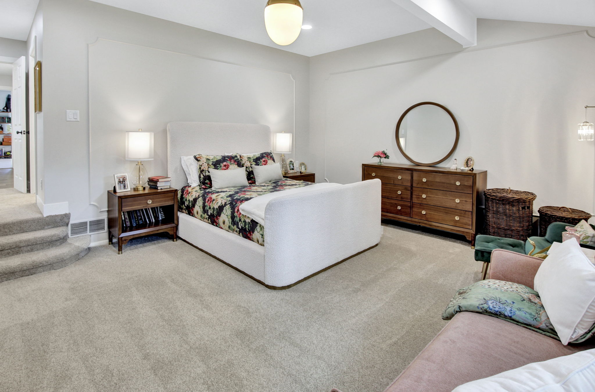 Spacious room featuring light-colored carpeting, a wall with decorative trim, a white upholstered headboard, and a built-in overhead light fixture