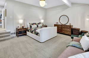 Spacious room featuring light-colored carpeting, a wall with decorative trim, a white upholstered headboard, and a built-in overhead light fixture