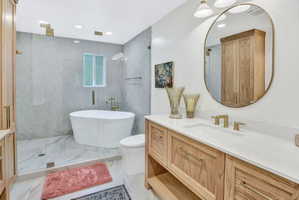 Spacious bathroom featuring a freestanding soaking tub, a walk-in shower with glass enclosure, a dual shower system, a wood-finish vanity with an integrated sink and gold-tone fixtures, and large-format tile flooring
