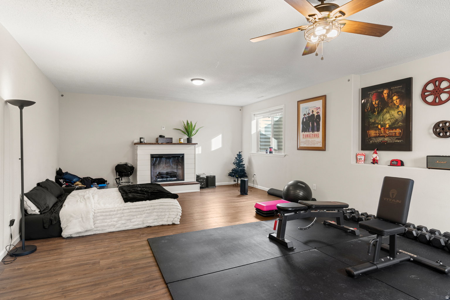 Spacious room featuring wood-finish flooring, a white-painted brick fireplace, and a ceiling fan with integrated lighting