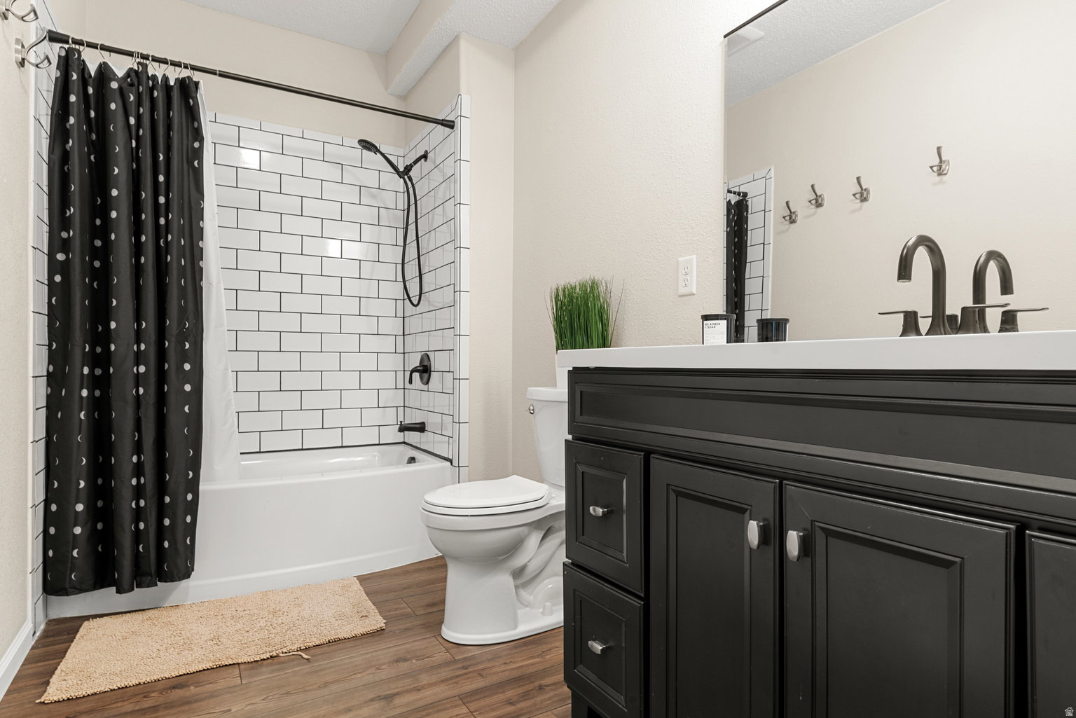 Bathroom featuring a dark wood-finish vanity with a white countertop, subway tile shower surround, matte black fixtures, and wood-finish flooring