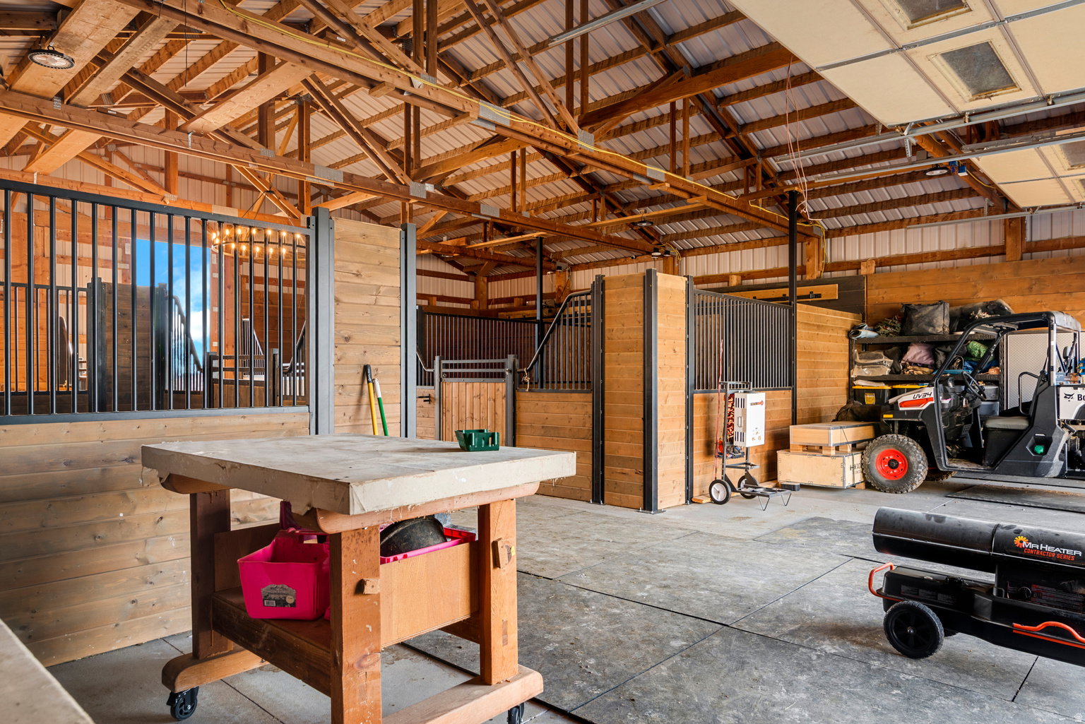 Barn interior featuring exposed timber ceiling trusses, corrugated metal roofing, and concrete flooring