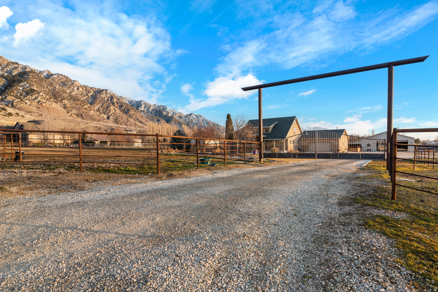 Gravel driveway entry featuring a metal archway and perimeter fencing