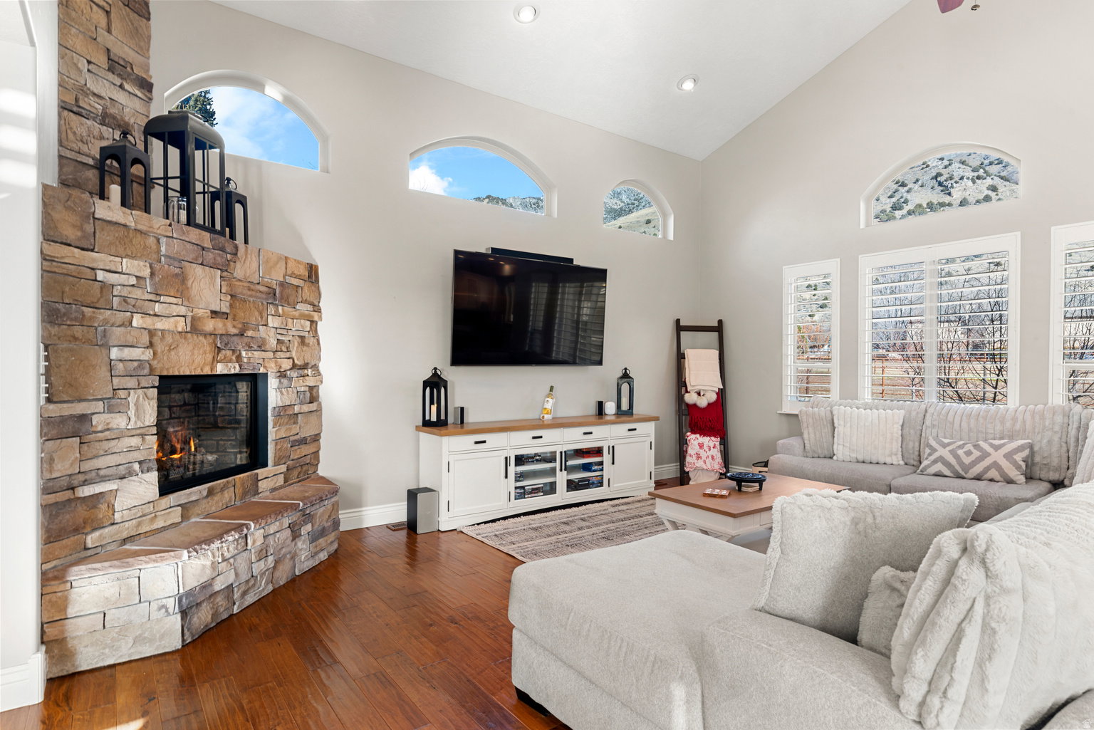 Spacious living area featuring a stone fireplace with hearth seating, vaulted ceilings, and wood-finish flooring