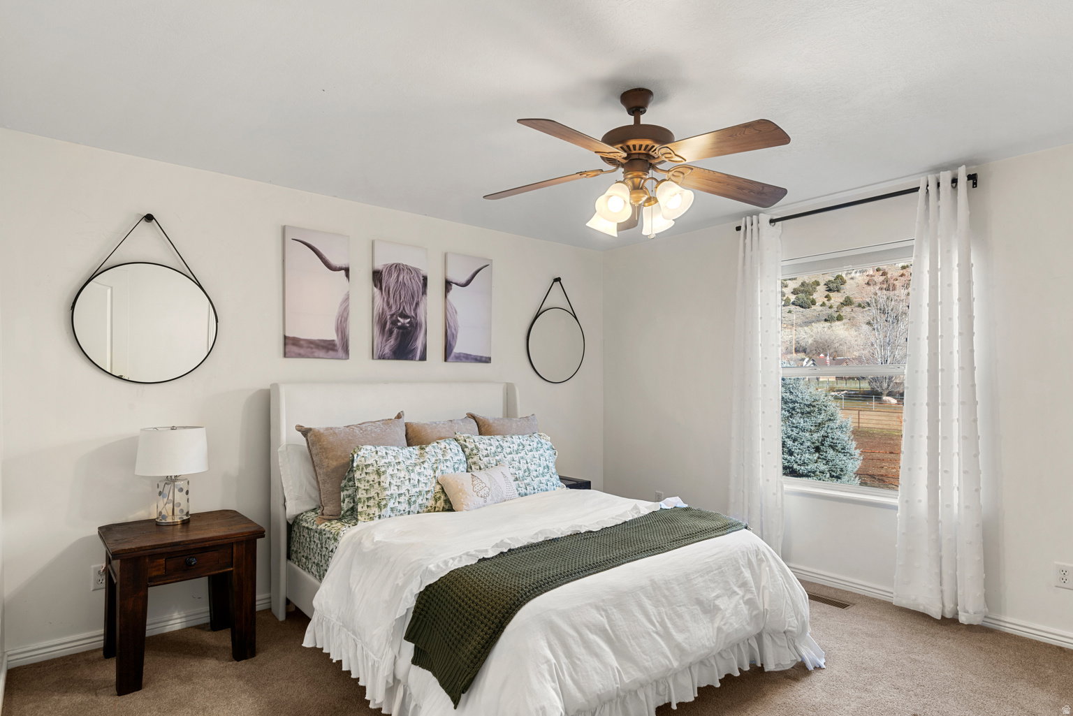 Carpeted bedroom featuring a ceiling fan with light fixture, a large window with white trim, and white walls