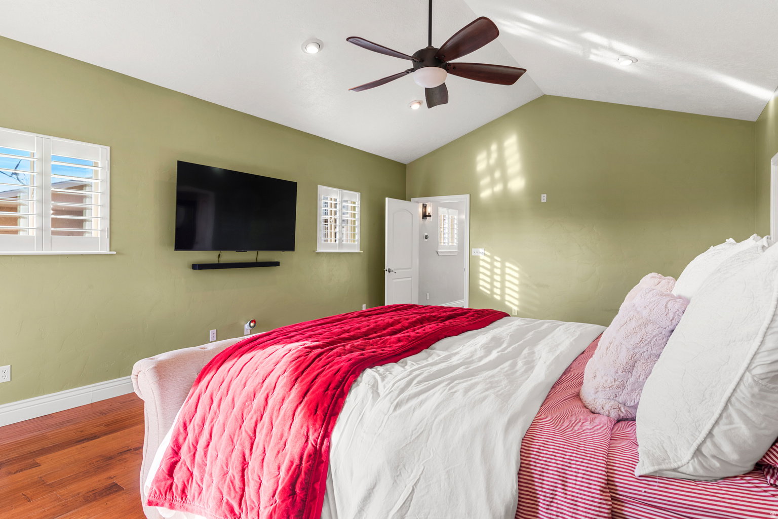 Vaulted ceiling room featuring wood-finish flooring, a ceiling fan with integrated lighting, and plantation shutters on multiple windows