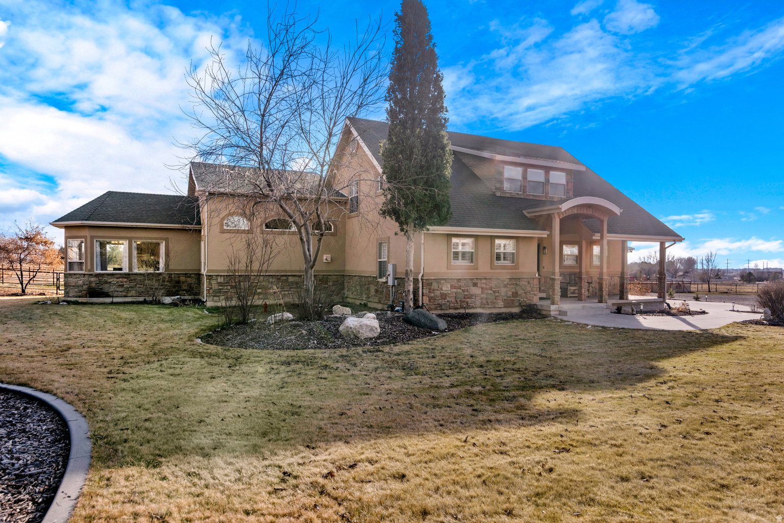 Stucco and stone exterior featuring multiple architectural elements, including arched windows, a covered front porch with wooden posts, and a dormer with three windows