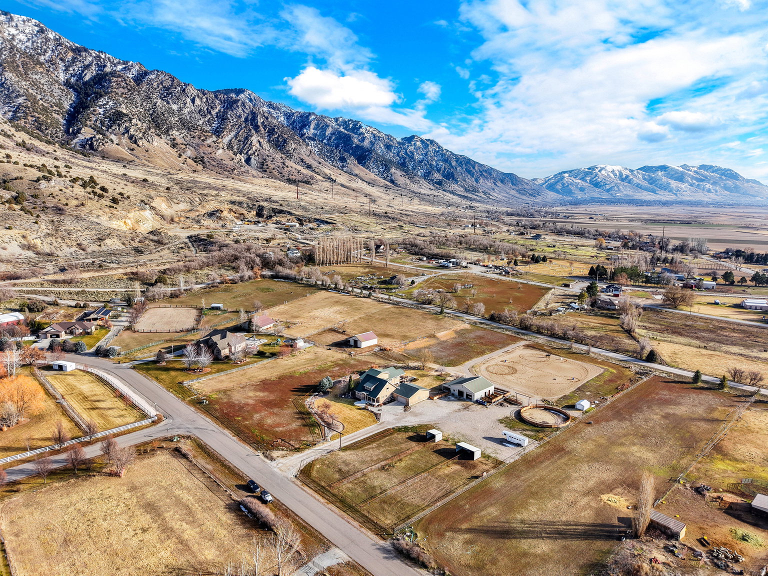 Expansive property featuring multiple structures, an equestrian round pen, open fields, and mountain scenery