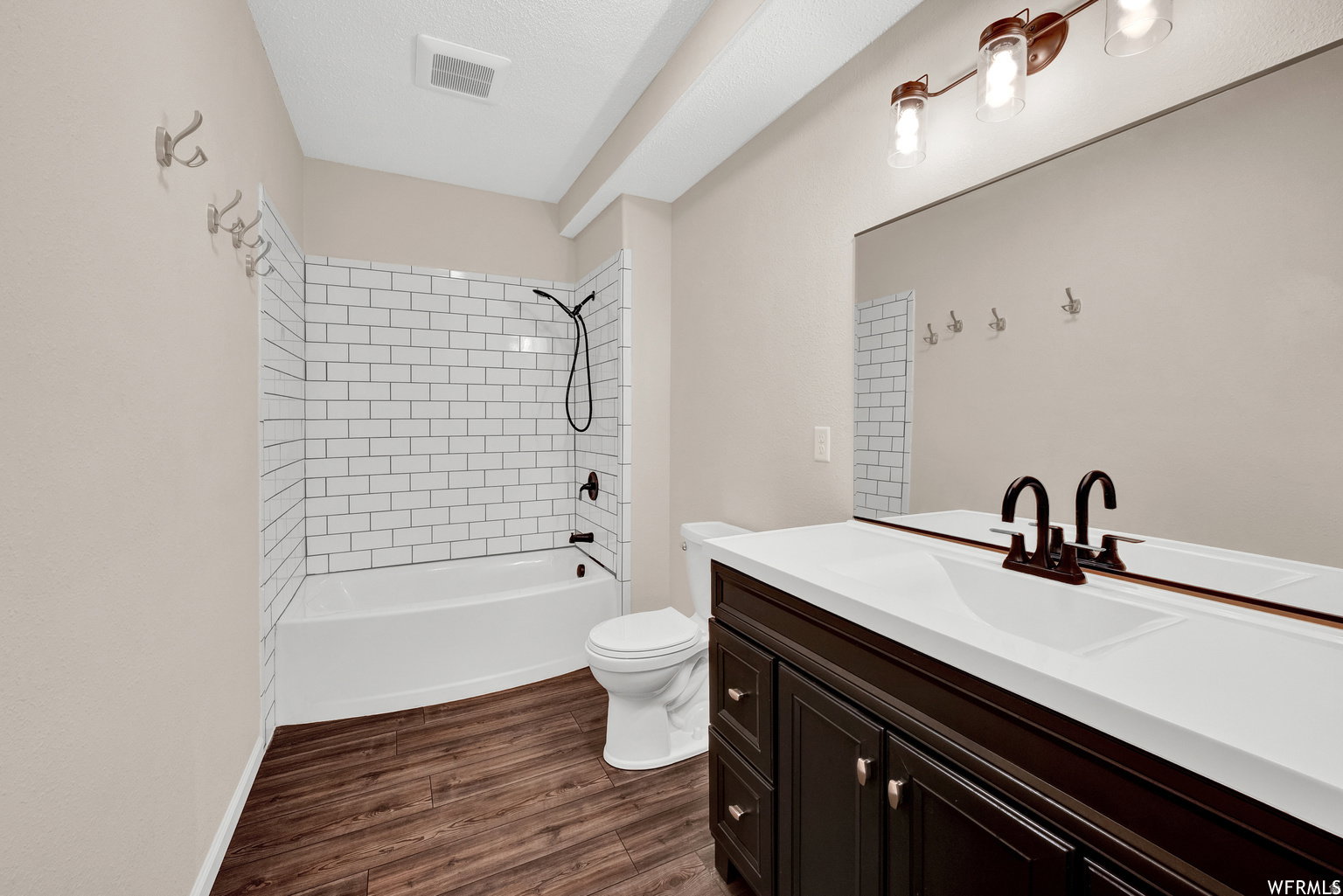 Bathroom featuring a dark wood-finish vanity with a white solid surface countertop, matte black fixtures, full-width mirror, and subway tile tub surround