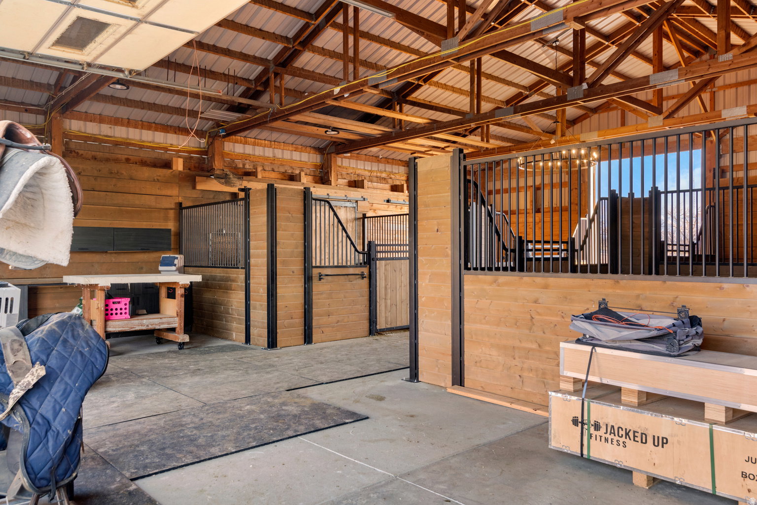 Barn interior featuring exposed wood beams, a metal roof, concrete flooring, and individual stalls with wood paneling and metal grates