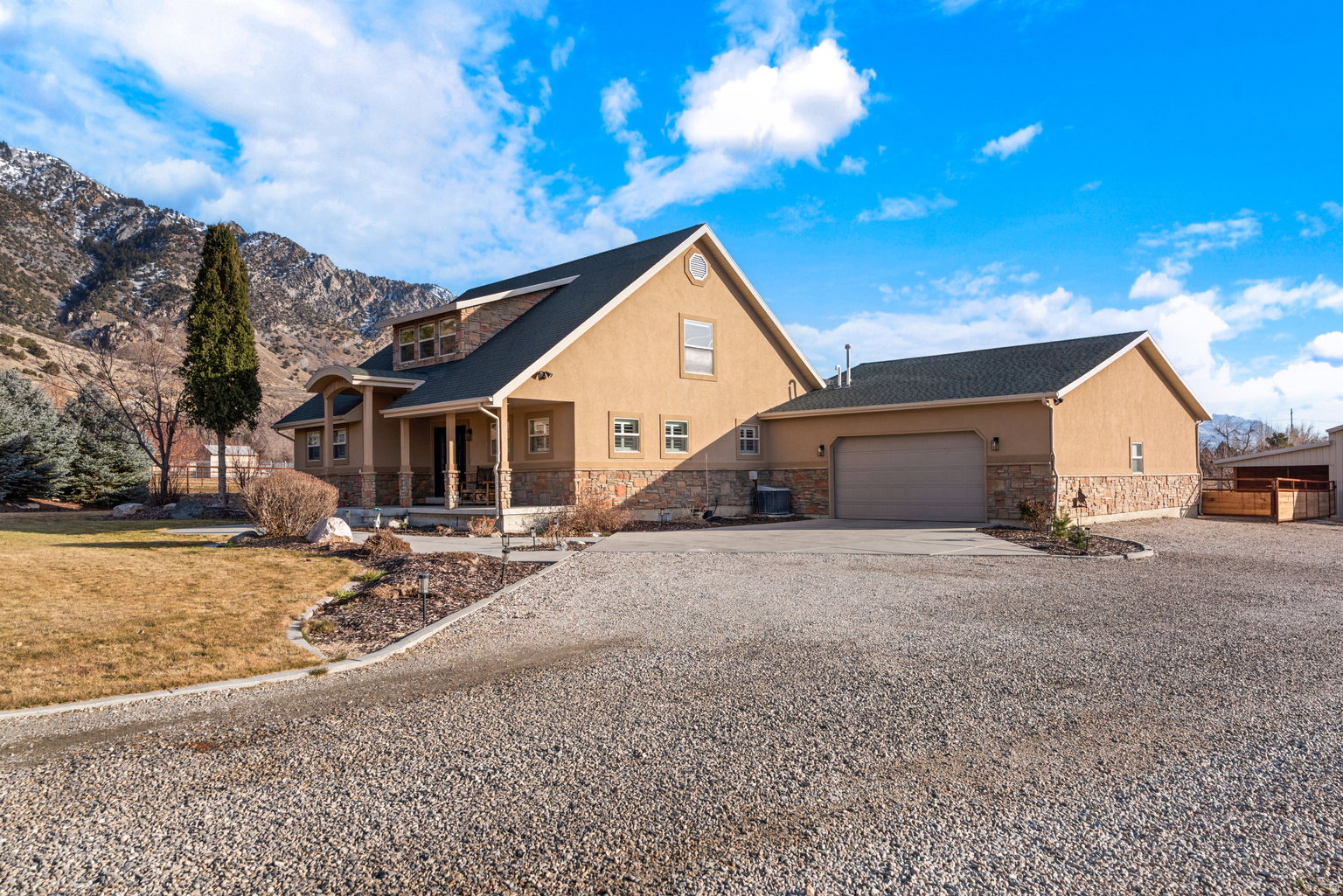 Two-story residence featuring a neutral-toned stucco exterior with stone accents, a covered front porch with columns, and an attached garage with a gravel driveway