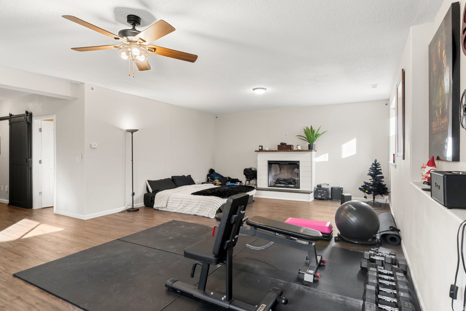 Spacious room featuring wood-finish flooring, a white brick fireplace with a wood mantle, and an overhead ceiling fan