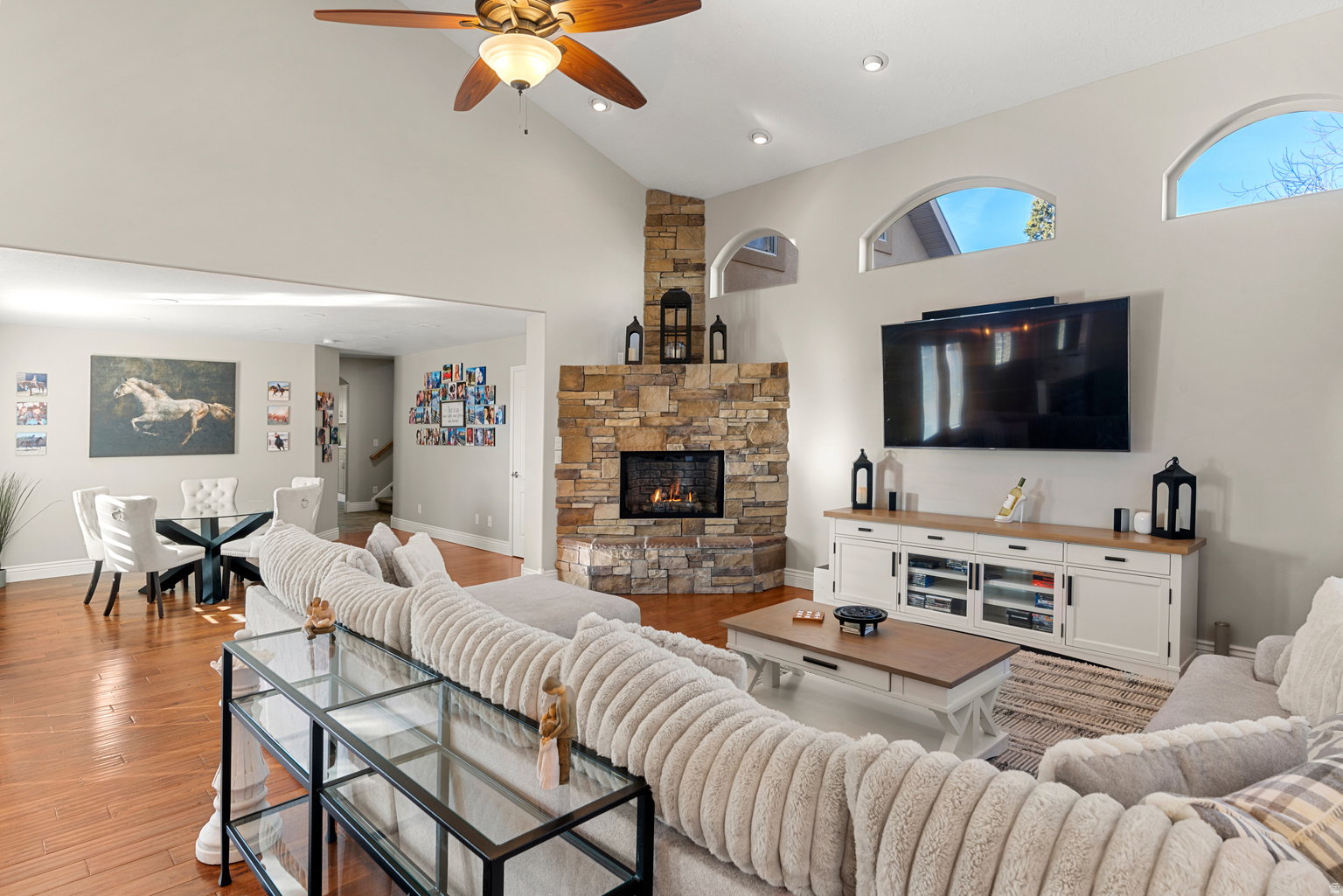 Spacious living area featuring wood-finish flooring, a stone-clad fireplace, and vaulted ceilings with a ceiling fan