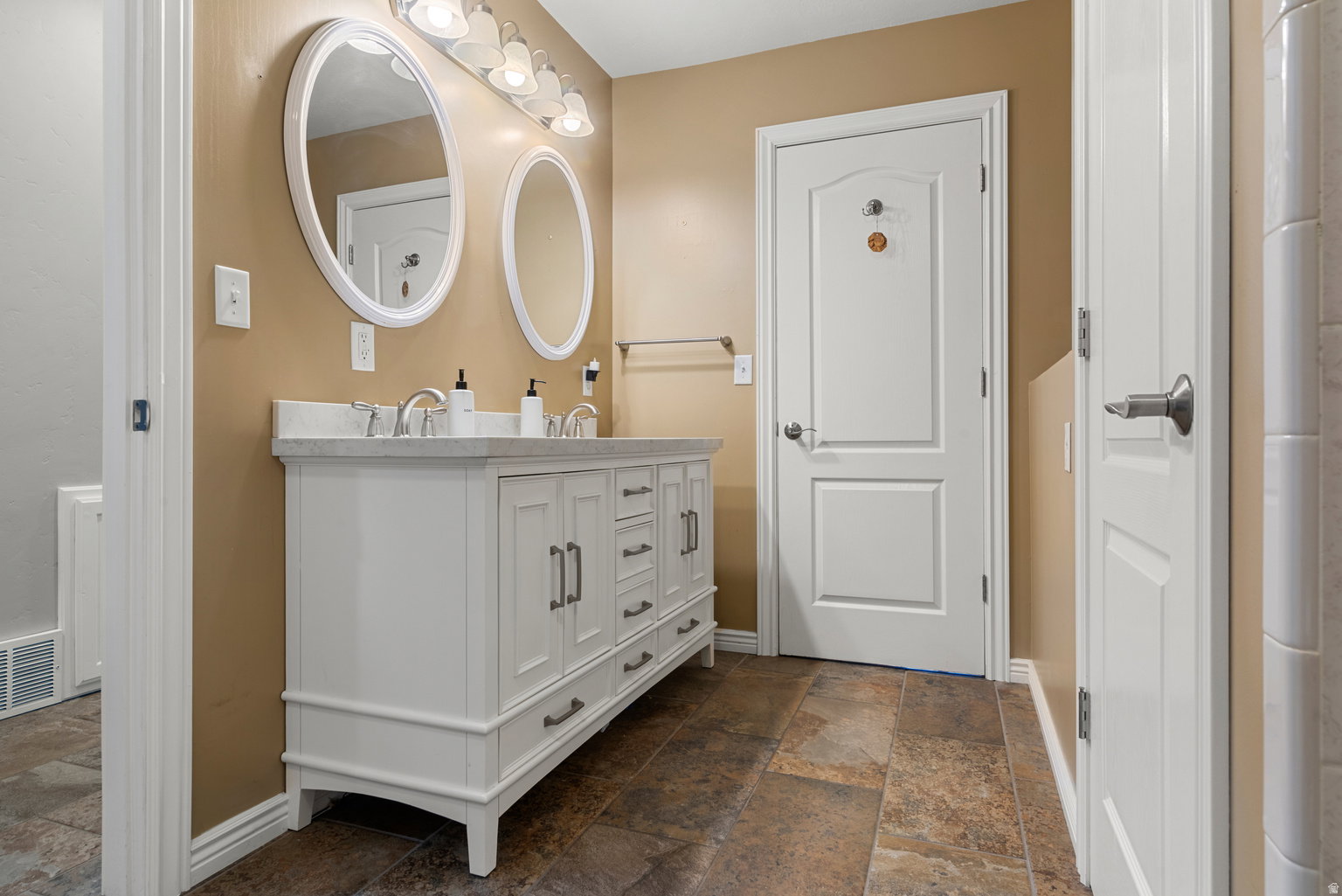 Bathroom featuring a white double vanity with dual oval mirrors, a light-colored countertop, and a six-light fixture