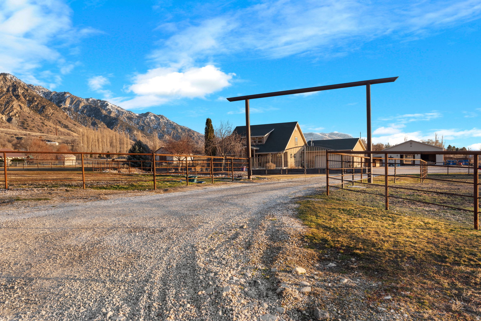 Gravel driveway leading to a residence with a gabled roof and an expansive fenced property