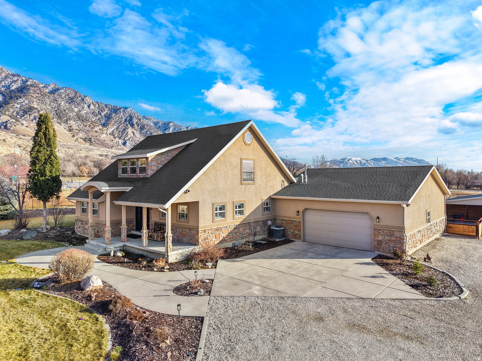Stucco and stone facade home featuring a covered front porch, a dormer with multiple windows, and a detached two-car garage