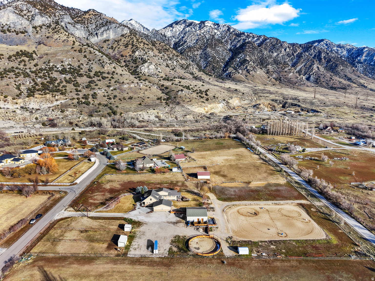 Expansive property featuring a main residence, multiple outbuildings, circular pen, and a riding arena, all set against a dramatic mountainous backdrop