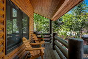 Covered porch featuring log-style railings, natural wood paneling, and a wood-plank ceiling