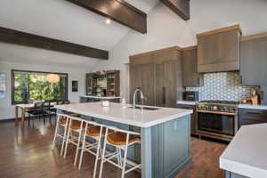 Vaulted ceiling kitchen featuring exposed wood beams, wood-finish flooring, a central island with countertop seating, and a built-in gas range with a hexagonal tile backsplash