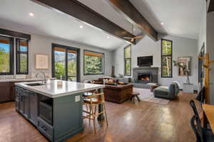 Open-concept living space featuring vaulted ceilings with exposed beams, wood-finish flooring, and a stone-clad fireplace