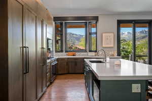 Modern kitchen featuring integrated appliances, a large center island with a sink, wood-finish flooring, and a range oven