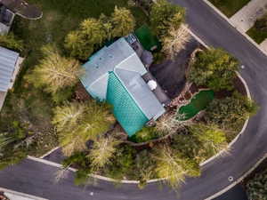 Property featuring a green metal roof, a paved driveway, and established landscaping with mature trees