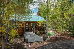 Log cabin exterior with a teal metal roof, a wooden ramp entrance, and an expansive front deck with log railings
